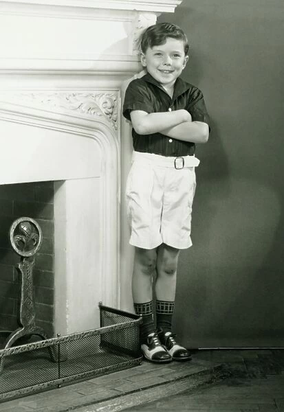 Young boy (6-7) standing by fireplace, (B&W)
