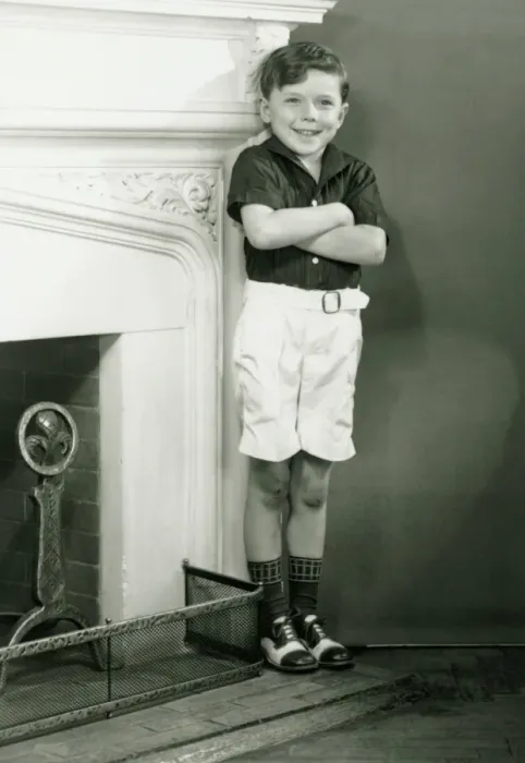 Framed Print : Young boy (6-7) standing by fireplace, (B&W) Framed Print : Young boy (6-7) standing by fireplace, (B&W)