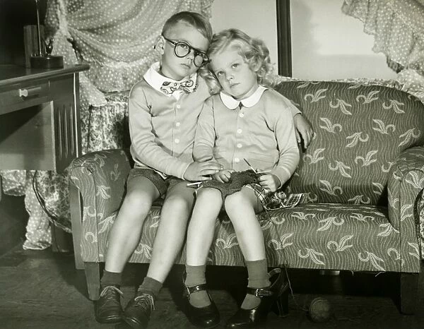 Young boy and girl dressed as adults sitting on sofa, portrait
