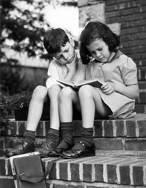 Young boy & girl reading a book outdoors