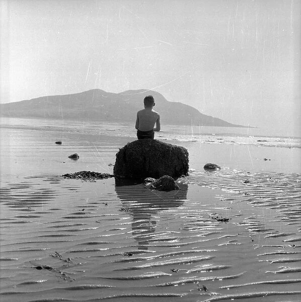 A young boy sitting on a rock in the sea just off the Isle of Arran