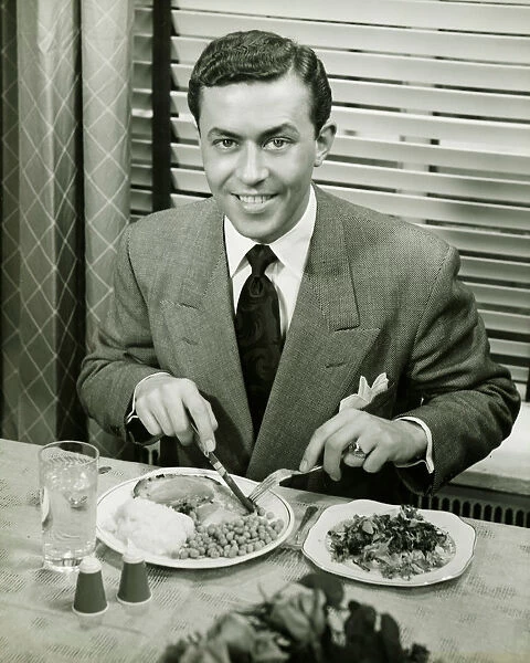 Young businessman eating dinner, (B&W), portrait