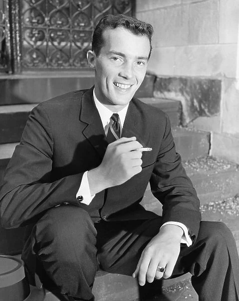 Young businessman sitting on steps, smoking cigarette, (B&W)