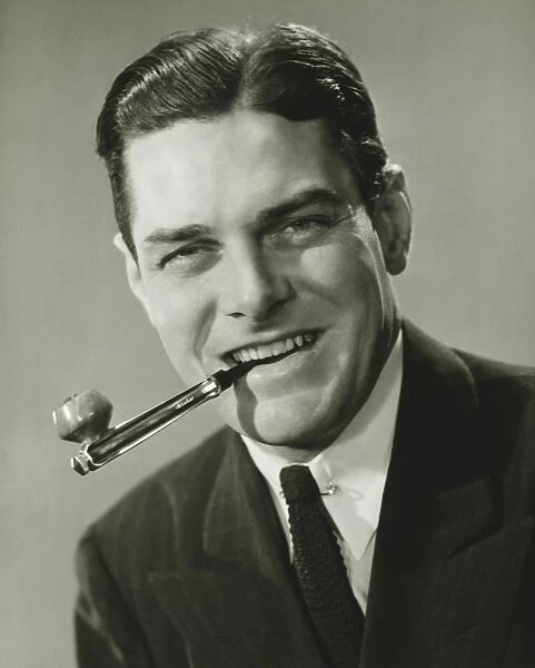 Young businessman in studio holding pipe in teeth, smiling, (B&W), portrait