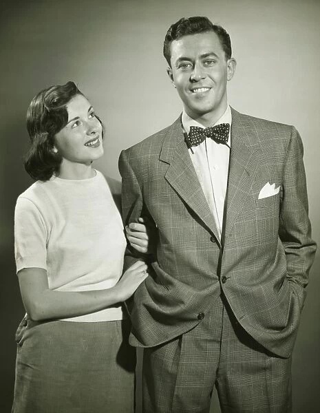 Young couple arm in arm in studio, woman looking at man, smiling, (B&W)