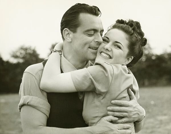 Young couple embracing in field, man kissing woman, (B&W)