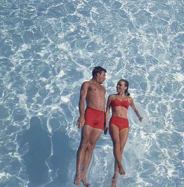Young couple jumping in swimming pool, smiling