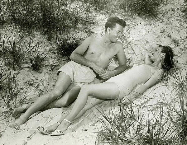 Young couple lying on sand, (B&W), elevated view