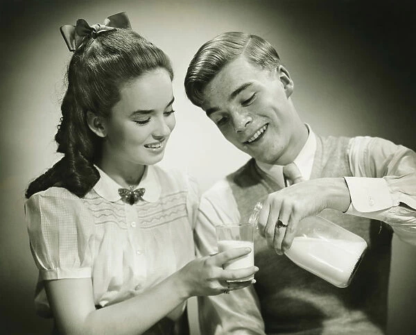 Young couple sharing bottle of milk, smiling, (B&W), close-up