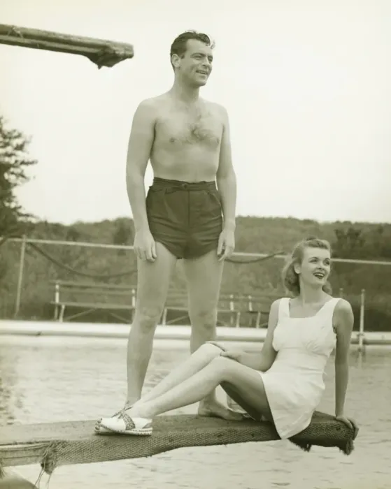Framed Print : Young couple on springboard, man standing, woman sitting, (B&W) Framed Print : Young couple on springboard, man standing, woman sitting, (B&W)
