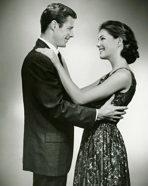 Young couple standing face to face, smiling, in studio, (B&W)