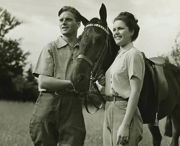Young couple standing with horse in field, (B&W)