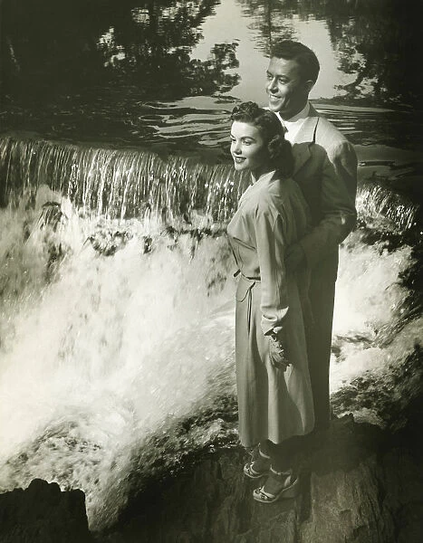 Young couple standing by waterfall, (B&W)