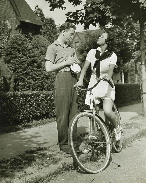 Young couple talking on street, woman on bicycle, (B&W)