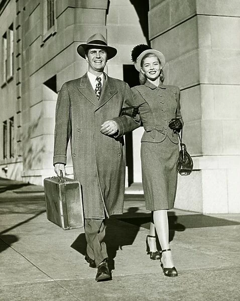 Young couple walking arm in arm on sidewalk, (B&W)