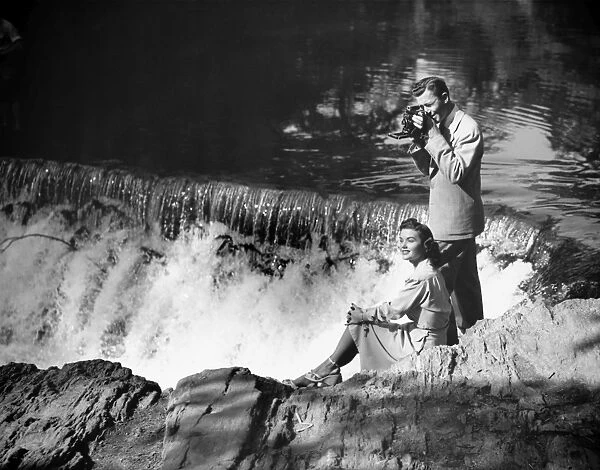 Young couple by waterfall, man taking picture, (B&W)