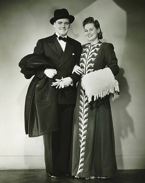 Young couple wearing formal dress standing in studio, (B&W)