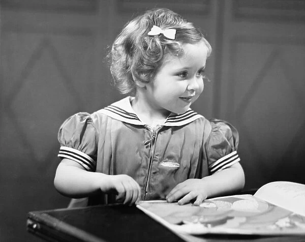 Young girl (4-5) at table reading book, (B&W)