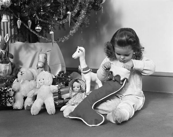 Young girl in pajamas, opening Christmas stocking next to Christmas tree. (Photo by H