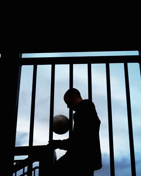 Young man with football by stairs and railing, silhouette