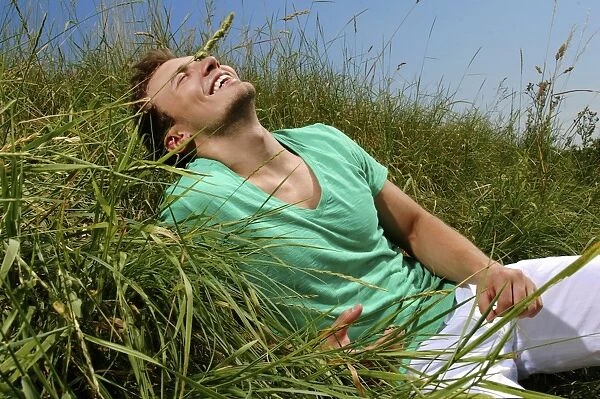 Young man lying in tall grass, smiling, sunbathing