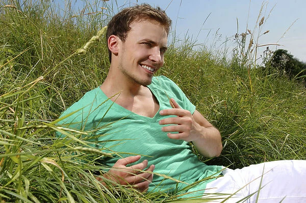 Young man lying in tall grass, smiling, sunbathing