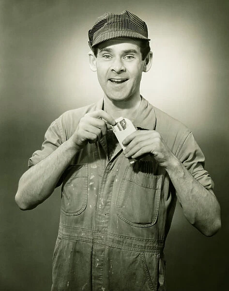 Young man in overalls showing card in studio, (B&W), portrait