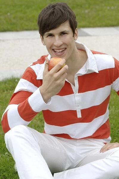 Young man sitting on a lawn eating an apple