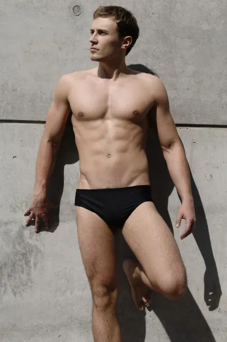 Framed Print : Young man wearing bathing trunks, leaning against a concrete wall