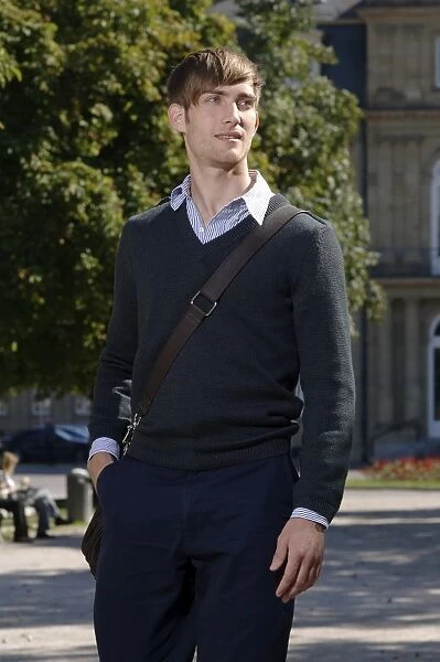 Young man wearing elegant clothing with a bag over his shoulder in front of the New Palace in Stuttgart, Baden-Wuerttemberg, Germany, Europe