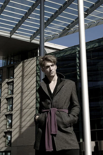 Young man wearing an overcoat in front of modern architecture, fashion shoot