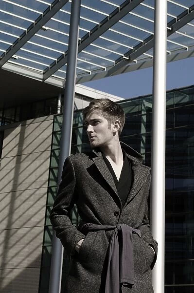 Young man wearing an overcoat in front of modern architecture, fashion shoot