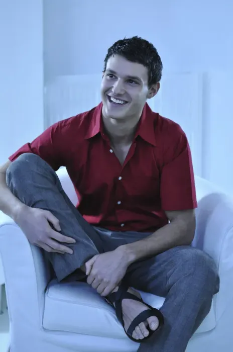 Framed Print : Young man wearing a red shirt sitting in an armchair, smiling Framed Print : Young man wearing a red shirt sitting in an armchair, smiling