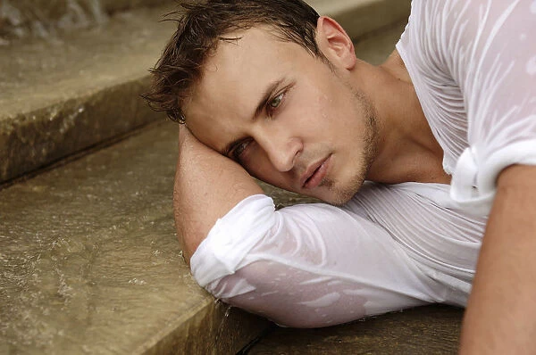 Young man wearing a wet shirt, lying on stairs