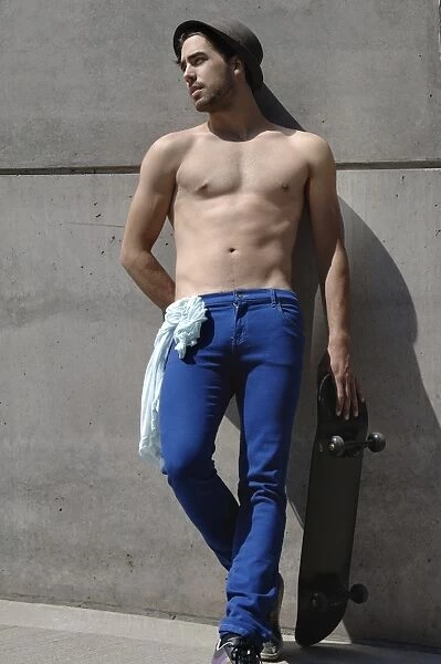 Young shirtless skater in front of a concrete wall