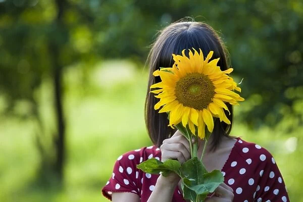Young woman, 25, holding a sunflower in front of her face