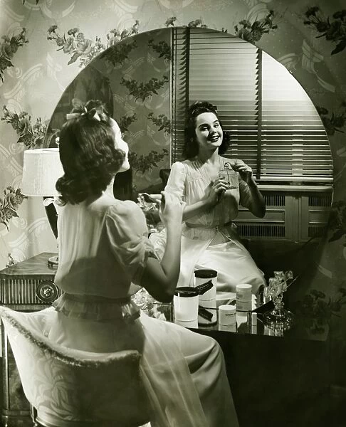 Young woman applying cream in front of mirror, (B&W)
