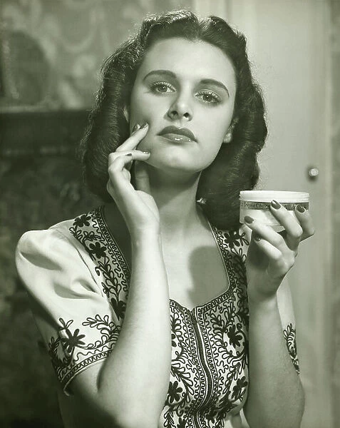 Young woman applying creme on face, (B&W), portrait