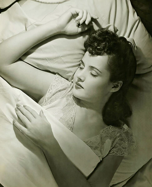 Young woman asleep on bed, (B&W), close-up