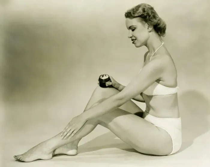 Framed Print : Young woman in bikini sitting, putting cream on leg, (B&W) Framed Print : Young woman in bikini sitting, putting cream on leg, (B&W)