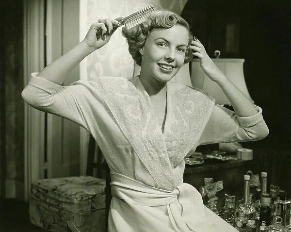 Young woman brushing hair, at home, (B&W), portrait