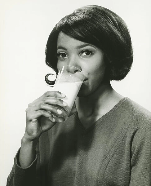 Young woman drinking milk in studio, smiling, (B&W), portrait