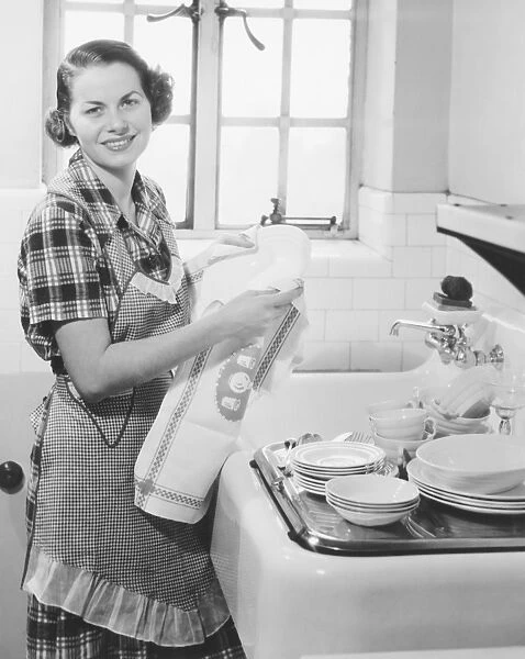 Young woman drying dishes in kitchen (B&W), portrait