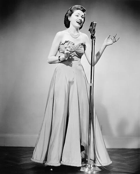 Young woman in evening dress at microphone, singing, (B&W)