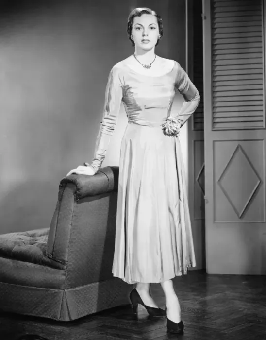 Framed Print : Young woman in evening dress standing, leaning against armchair, (B&W)