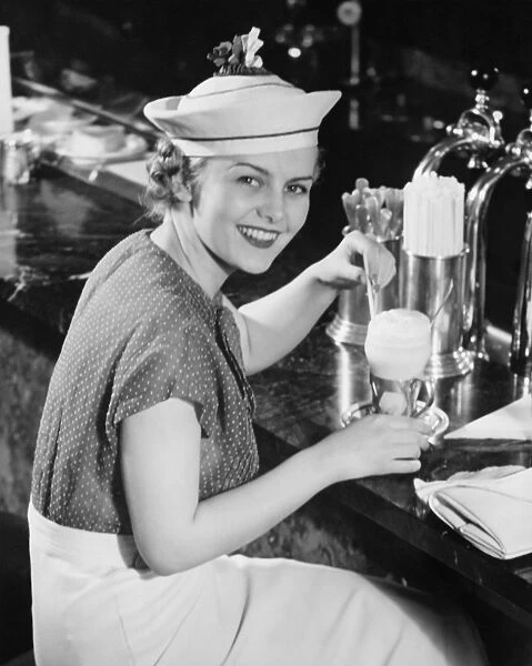 Young woman in fancy hat drinking ice cream soda (B&W), portrait