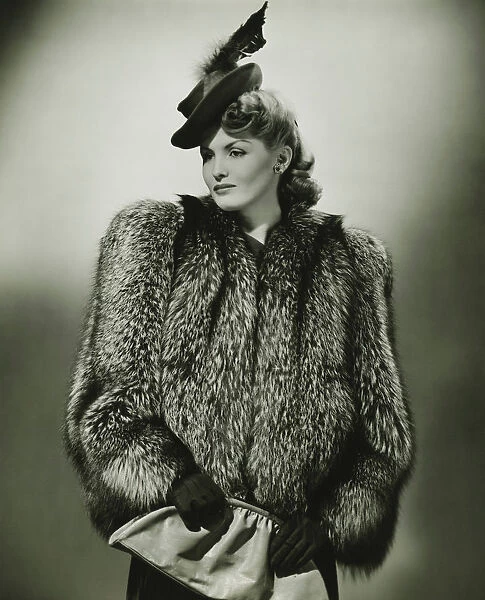 Young woman in fur coat and fashionable hat in studio, (B&W)