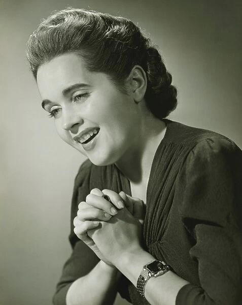 Young woman with hands put together smiling in studio (B&W), close-up