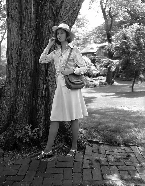 Young woman in hat standing by tree, (B&W)