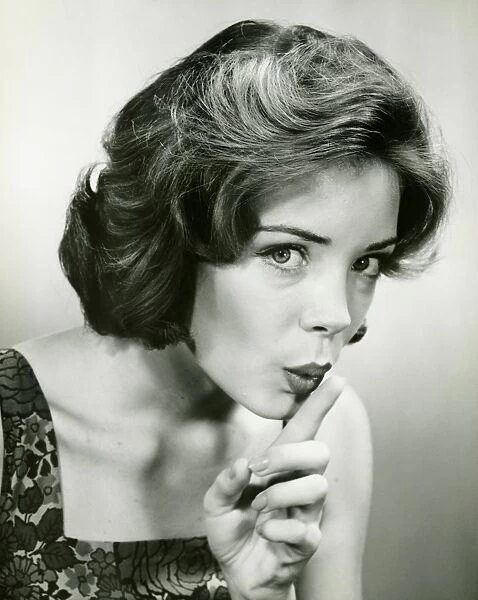 Young woman holding finger on lips, posing in studio, (B&W), (Portrait)